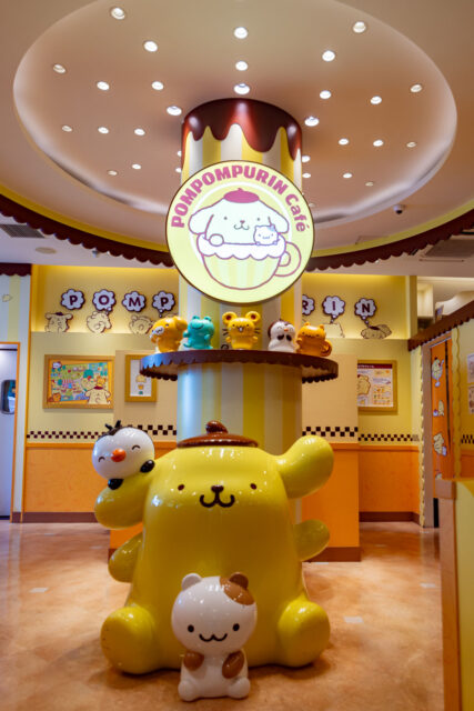 Interior of the Pompompurin Café in Harajuku, Tokyo, decorated in bright yellow with large statues of Pompompurin and friends, creating a playful Sanrio-themed atmosphere.