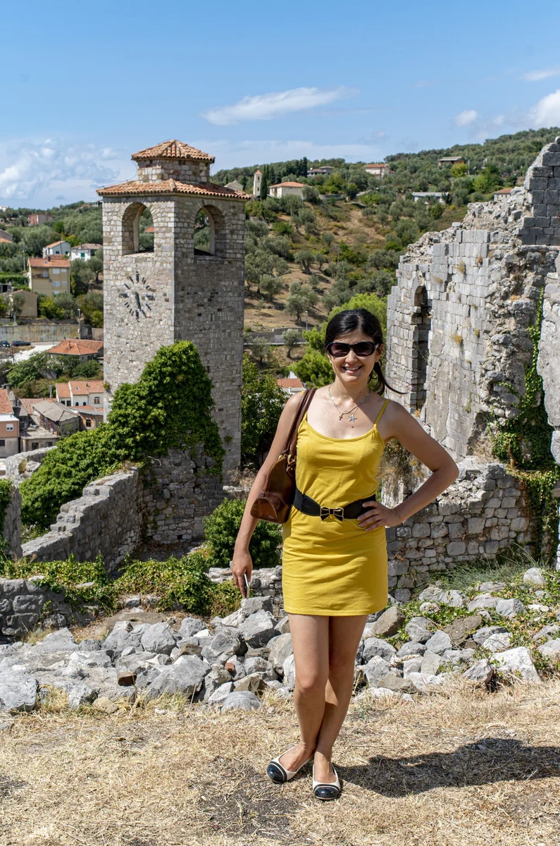 Travel blogger Ket standing in front of the medieval clock tower and stone ruins of Stari Bar, Montenegro