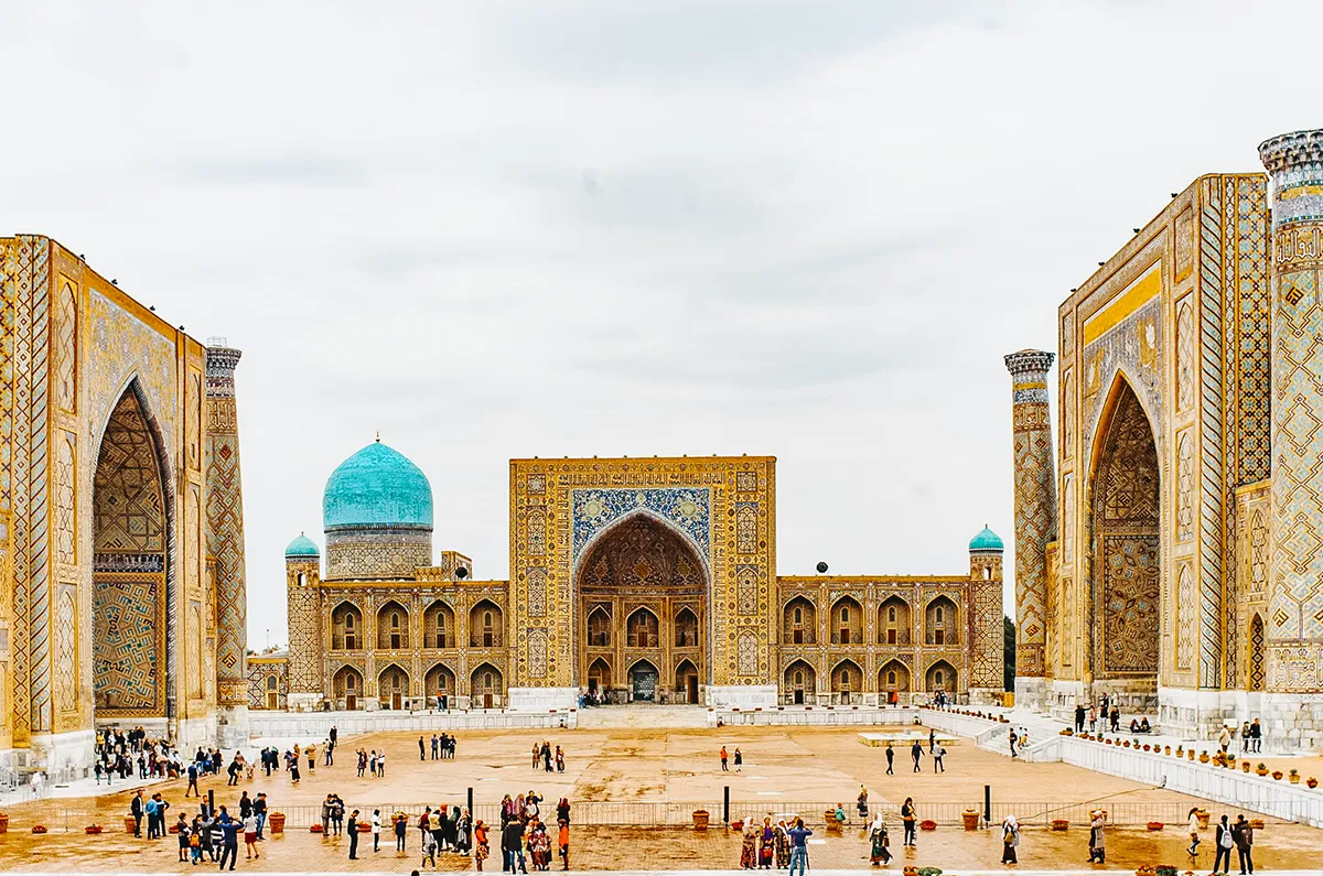 Registan Square in Samarkand with three madrasas and tourists in the courtyard