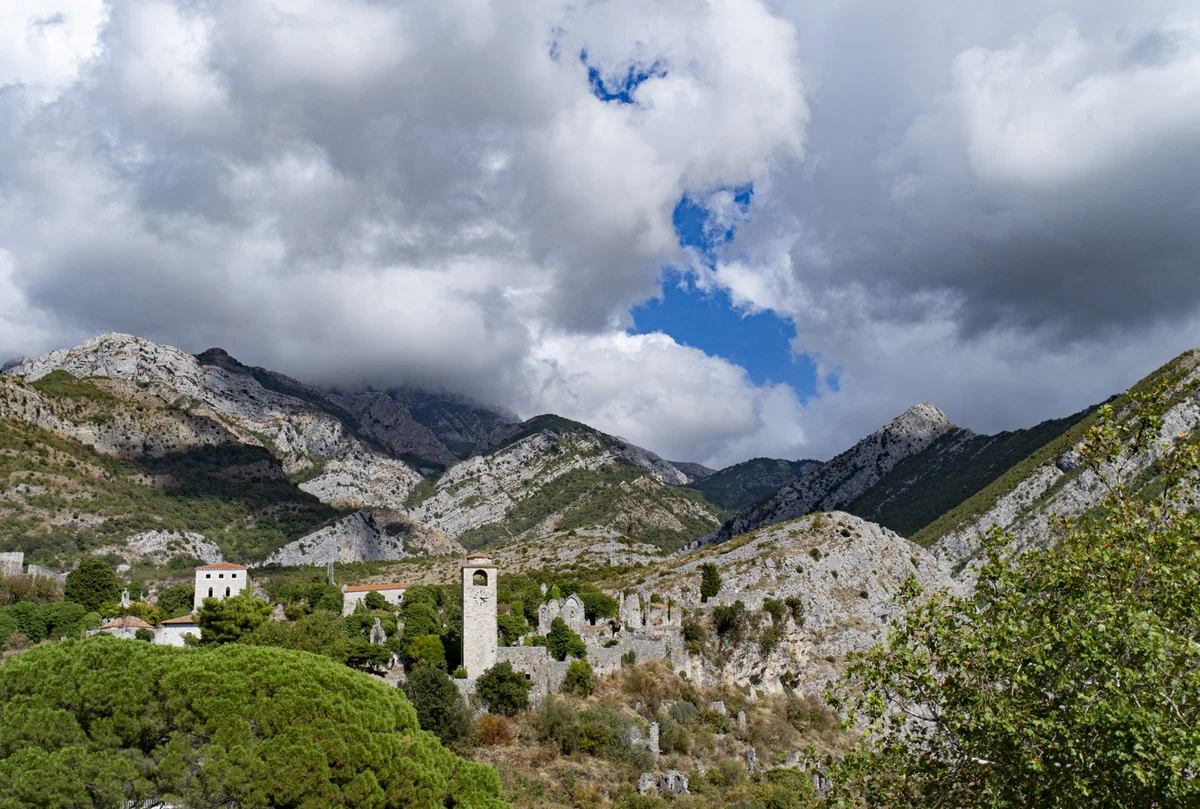 Distant view of Stari Bar ruined fortress and clock tower nestled at the foot of dramatic rocky mountains, Montenegro